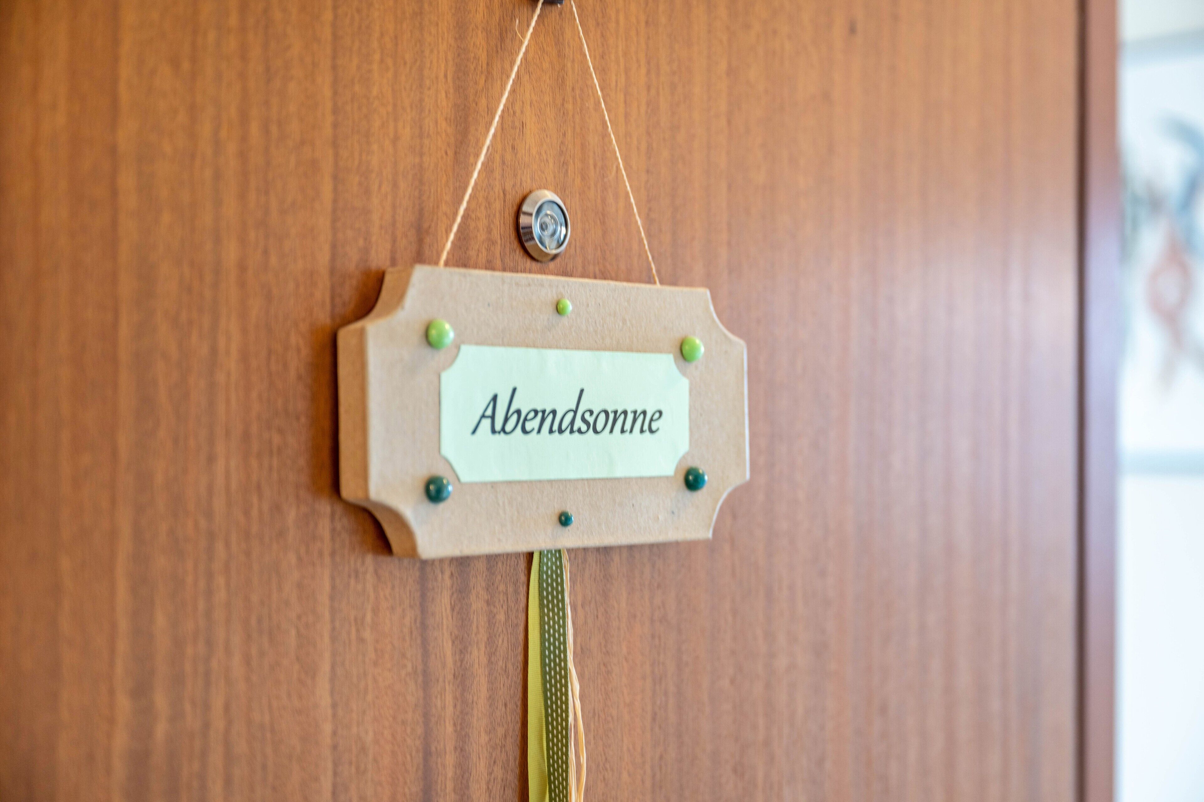 Une porte en bois sur laquelle est accroché un panneau indiquant « Abendsonne », et un petit objet décoratif suspendu en haut.