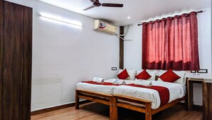 Une chambre d’hôtel avec un lit en bois, une literie rouge et blanche, un ventilateur de plafond et une fenêtre avec des rideaux rouges.