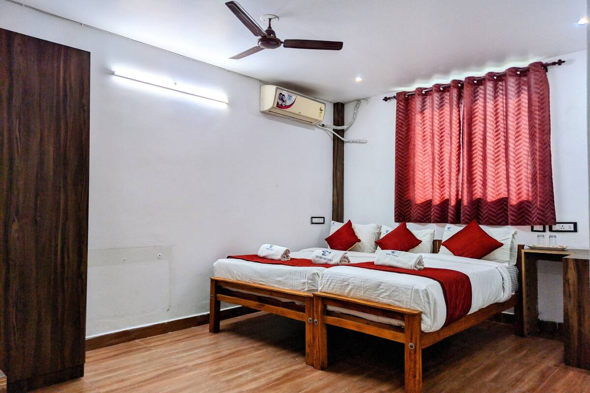 Une chambre d’hôtel avec un lit en bois, une literie rouge et blanche, un ventilateur de plafond et une fenêtre avec des rideaux rouges.