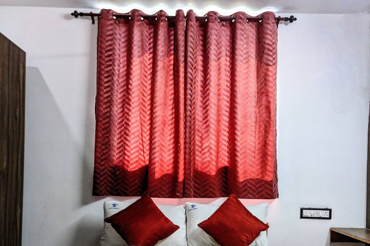 Une chambre d’hôtel avec un lit, des rideaux rouges et deux oreillers ornés du logo de l’hôtel.