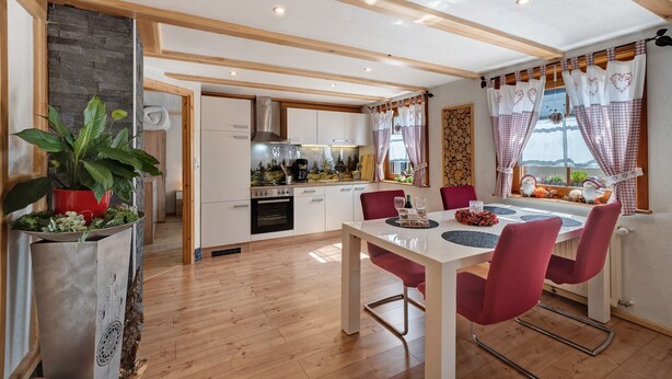 A modern kitchen with wooden beams, a dining area with red chairs, and a view of the outdoors. - Apartment 'Steinbühlschlössle' with Shared Terrace, Shared Garden and Wi-Fi (Schönwald im Schwarzwald)