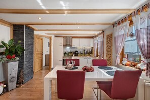 A modern kitchen with wooden beams, a stone accent wall, and a dining area with red chairs. - Apartment 'Steinbühlschlössle' with Shared Terrace, Shared Garden and Wi-Fi (Schönwald im Schwarzwald)