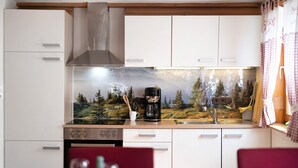 A compact kitchen with white cabinets, a stainless steel range hood, a coffee maker, and a scenic mountain wallpaper. - Apartment 'Steinbühlschlössle' with Shared Terrace, Shared Garden and Wi-Fi (Schönwald im Schwarzwald)