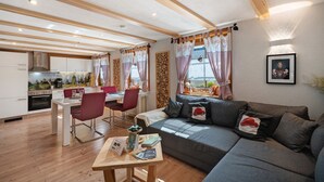 A modern living room with a sofa, dining table, chairs, and a kitchen in the background. - Apartment 'Steinbühlschlössle' with Shared Terrace, Shared Garden and Wi-Fi (Schönwald im Schwarzwald)