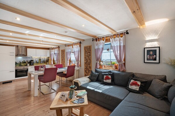 A modern living room with a sofa, dining table, chairs, and a kitchen in the background. - Apartment 'Steinbühlschlössle' with Shared Terrace, Shared Garden and Wi-Fi (Schönwald im Schwarzwald)