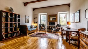 A spacious living room with a wooden floor, a sofa, a fireplace, and a dining area. - GuestHost - Porta Romana Charme Apartment (Siena)
