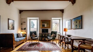 A living room with a sofa, chairs, a dining table, a rug, a bookshelf, and a fireplace. - GuestHost - Porta Romana Charme Apartment (Siena)