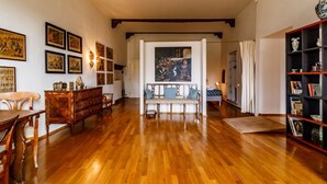 A spacious room with wooden flooring, a sofa, a dining table, and a bookshelf. - GuestHost - Porta Romana Charme Apartment (Siena)