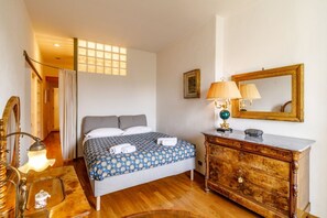 A bedroom with a bed, wooden dresser, lamp, and a mirror.