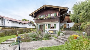 A traditional chalet with a stone pathway, a wooden balcony with plants, and a bench outside.