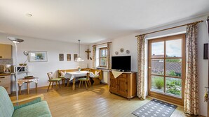 A living room with a sofa, a dining table with chairs, a TV, and a window with curtains.