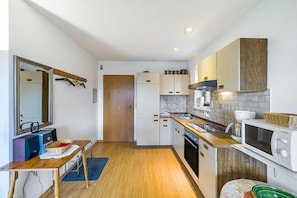 A compact kitchen with wooden cabinets, a microwave, a stove, and a sink. - Apartment 'Kauderer - Wohnung 1' with Private Terrace, Shared Garden and Wi-Fi (Waging am See)