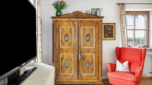 A room with a wooden wardrobe, a red armchair, and a window with curtains.