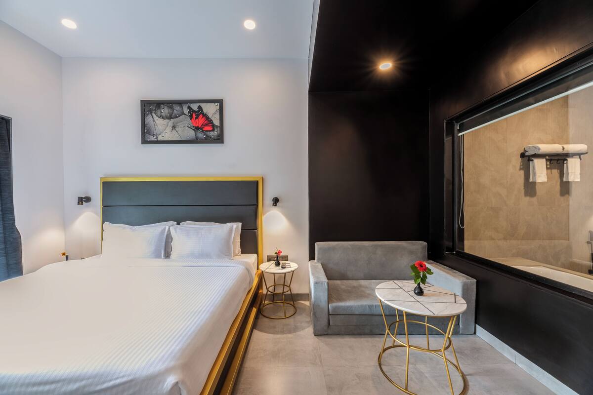 Una camera d'albergo moderna con un letto grande, un tavolino rotondo, una poltrona grigia e un'ampia finestra vista vasca da bagno.