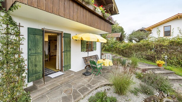A traditional chalet with a stone staircase, a wooden balcony with flower boxes, and a small outdoor seating area with a yellow umbrella. - Apartment 'Kauderer - Wohnung 2' with Private Terrace, Shared Garden and Wi-Fi (Waging am See)