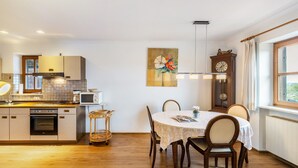 A kitchen with wooden cabinets, a dining table with chairs, a clock, and a window with a view. - Apartment 'Kauderer - Wohnung 2' with Private Terrace, Shared Garden and Wi-Fi (Waging am See)