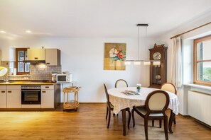 A kitchen with wooden cabinets, a dining table with chairs, a clock, and a window with a view.