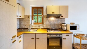A kitchen with wooden cabinets, a built-in oven, a microwave, and a window with a view of greenery. - Apartment 'Kauderer - Wohnung 2' with Private Terrace, Shared Garden and Wi-Fi (Waging am See)