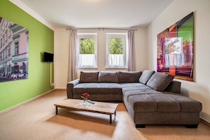 Ein Wohnzimmer mit einer Eckcouch, einem Couchtisch, einem Flachbildfernseher und einem Bild an der Wand.
