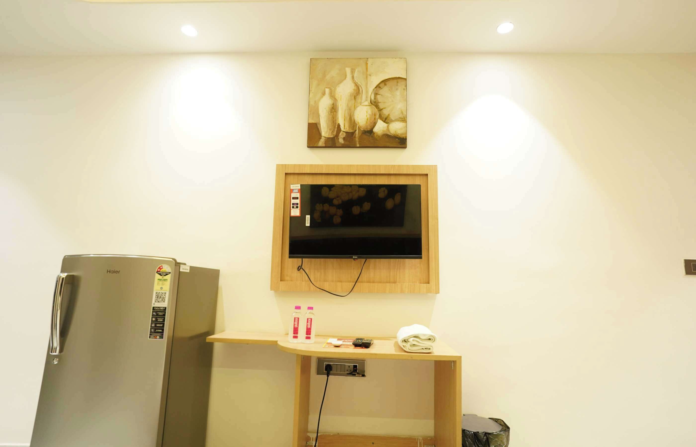 A compact kitchen with a refrigerator, a wooden countertop, a television mounted on the wall, and a painting above the TV.
