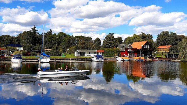 A calm lake with boats, a dock, and houses in the background.