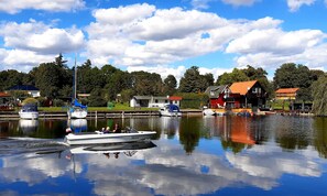 Un lago tranquilo con barcos, un muelle y casas al fondo.