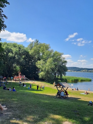 Un parque con un parque infantil, zonas verdes y un lago.