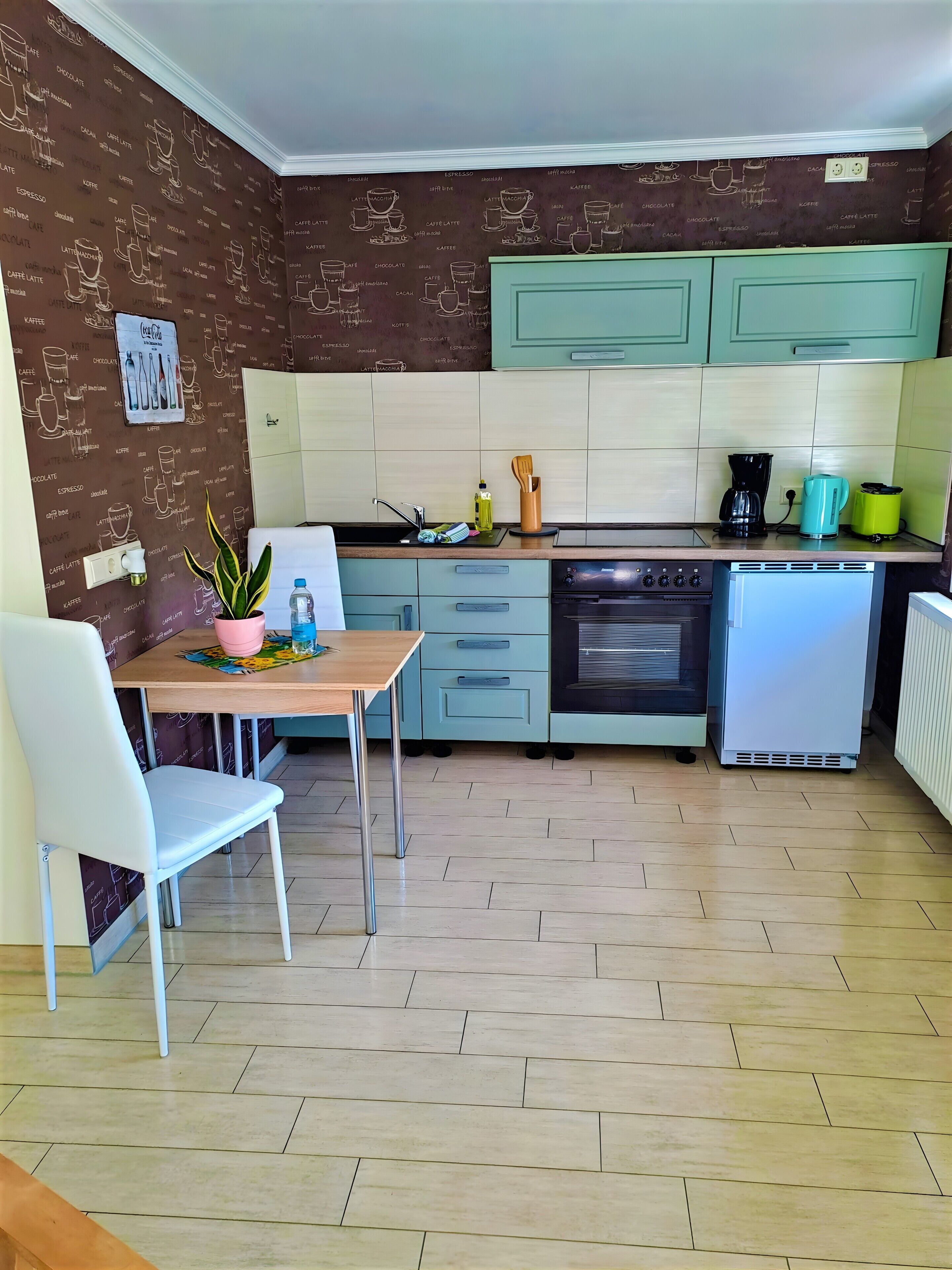 Cocina compacta con comedor, que incluye cafetera, hervidor y refrigerador pequeño.