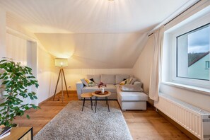 Un salon confortable avec un canapé, une table basse, une lampe et une grande fenêtre.
