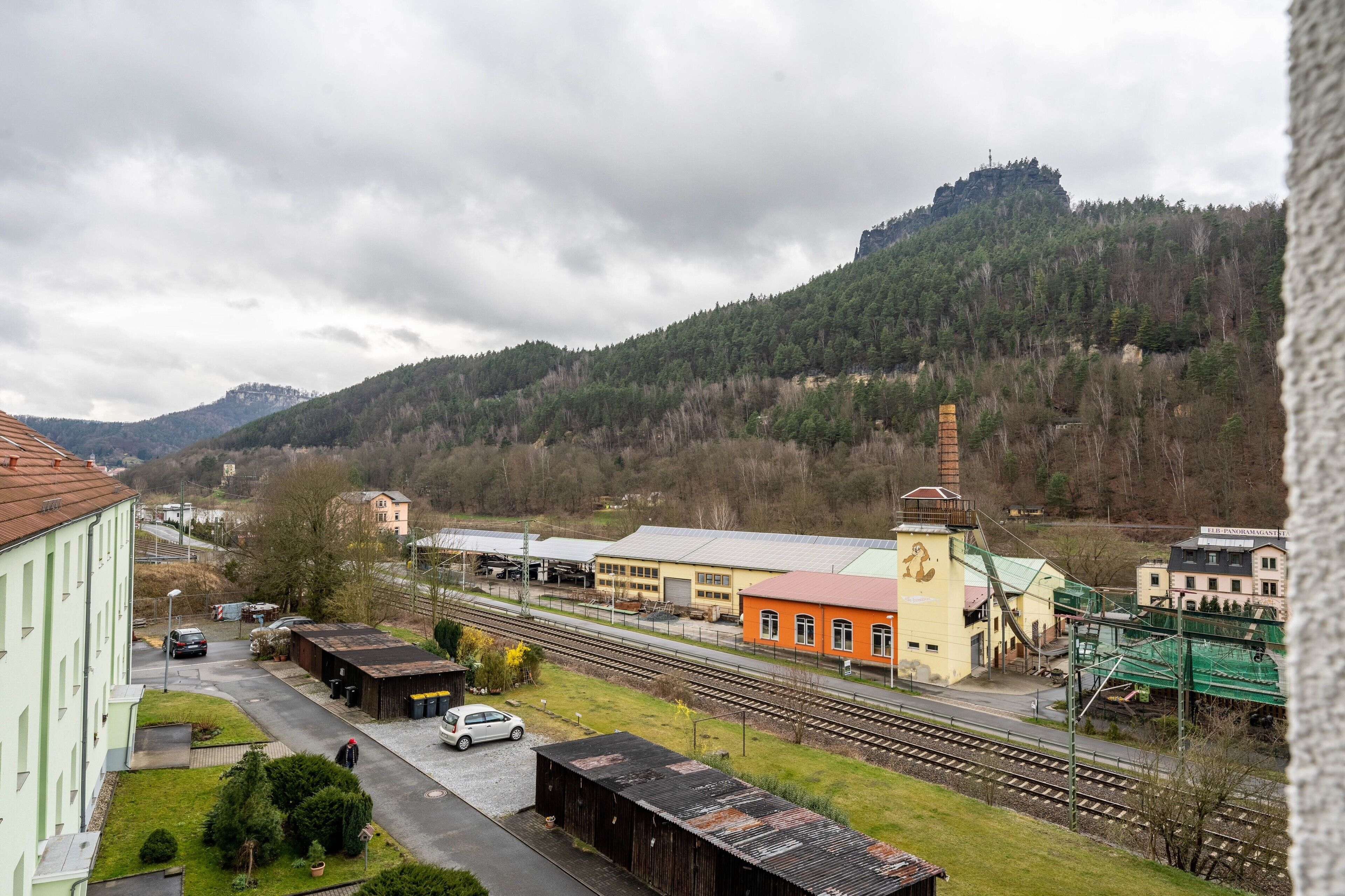 A railway station with buildings, a train track, and a hill in the background.
