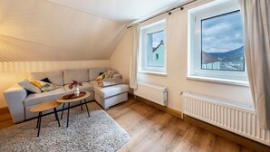 Un dormitorio tipo loft acogedor, con un ventanal grande, un sofá, una mesita y un radiador.