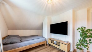 Un dormitorio con una cama, televisión, planta y suelo de madera.