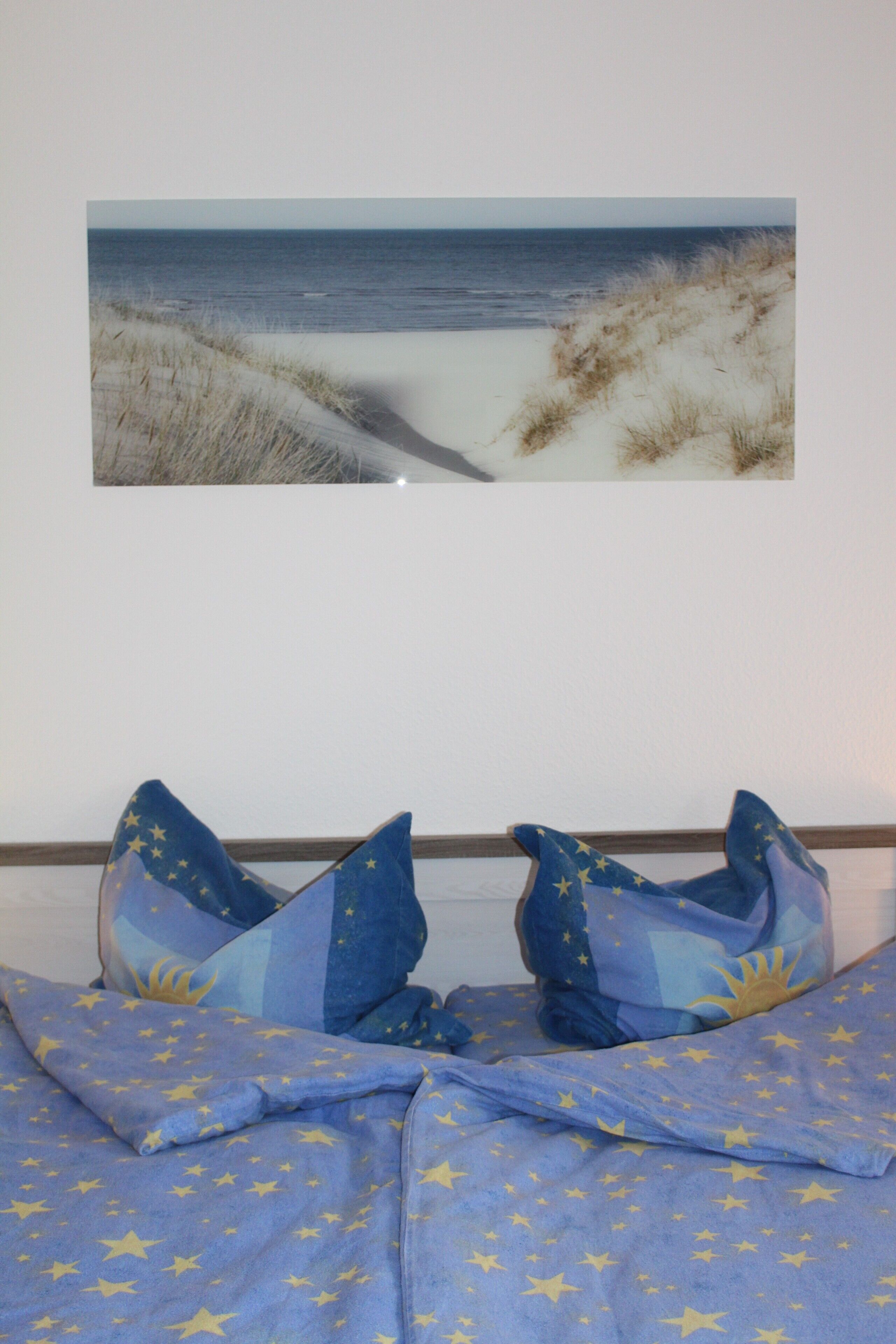 Une chambre à coucher avec un lit, des oreillers et un tableau représentant une plage, accroché au mur.