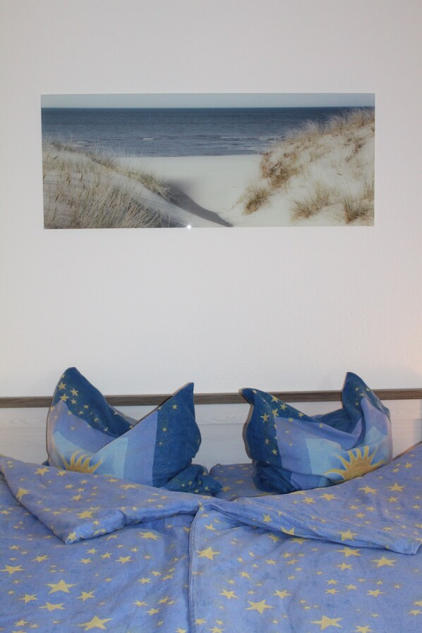 A bedroom with a bed, pillows, and a wall-mounted picture of a beach.