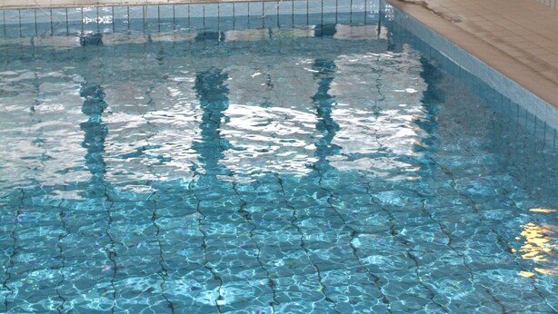 Une piscine intérieure à l’eau claire, avec des murs carrelés et des fenêtres donnant sur la verdure.