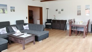 Un salon avec un canapé, une table basse et une table à manger. Le plafond est orné de poutres en bois et une lampe se trouve dans un coin.