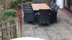 Une terrasse extérieure avec une table et des chaises en bois, une clôture en bois et un bâtiment en briques en arrière-plan.