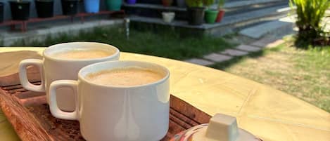 Una bandeja con tres tazas blancas, una tetera colorida y dos cucharas blancas sobre una mesa de madera.