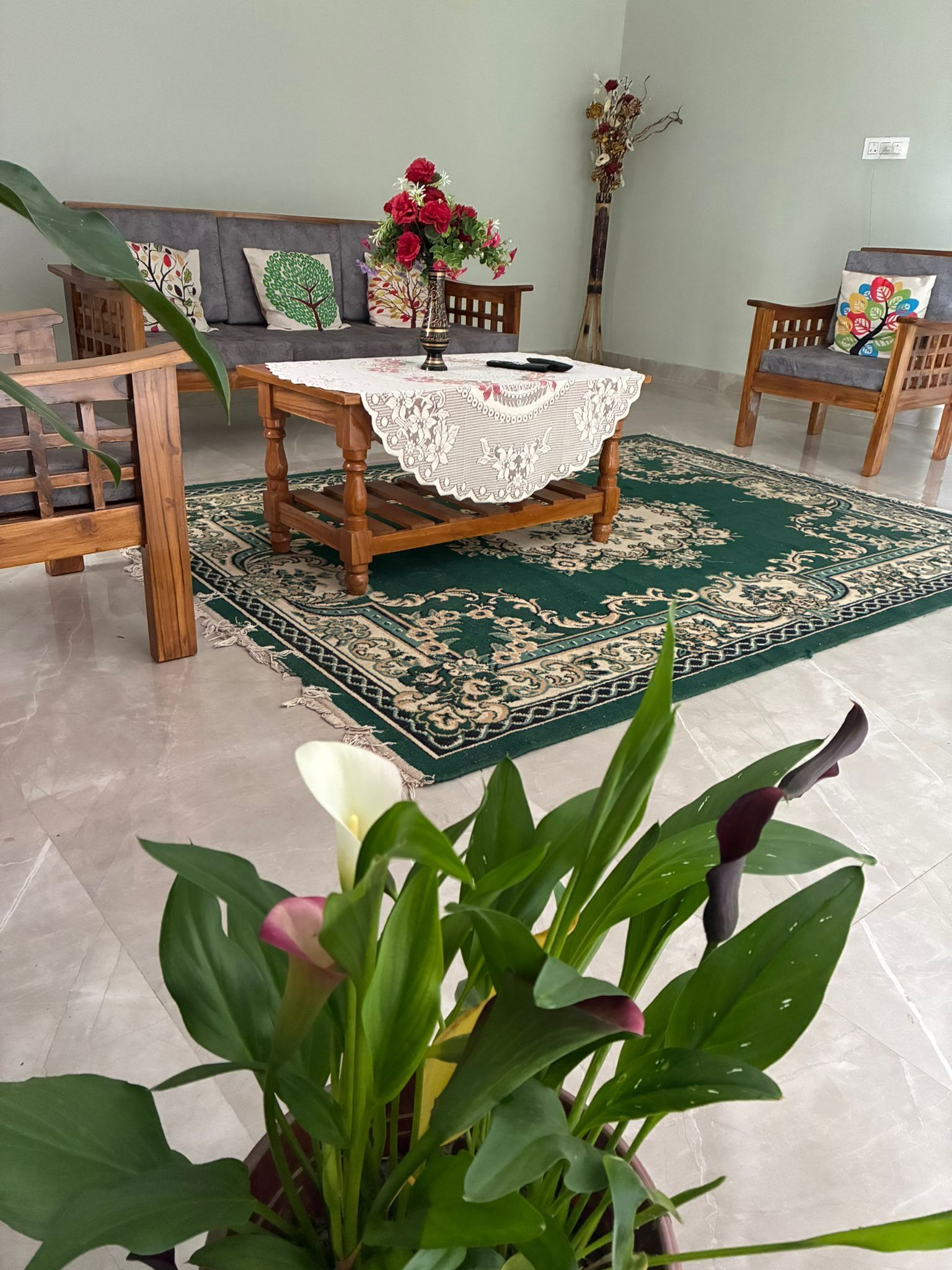 Una sala de estar con una mesa de centro de madera, un tapete estampado en verde y un sofá con almohadones decorativos.
