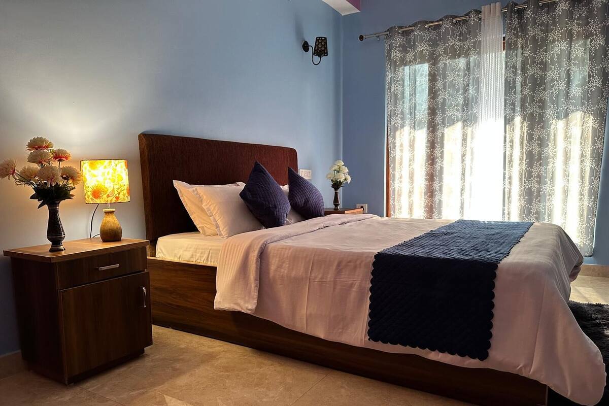 Un dormitorio con cama de madera, una mesita de noche con lámpara y un jarrón de flores.