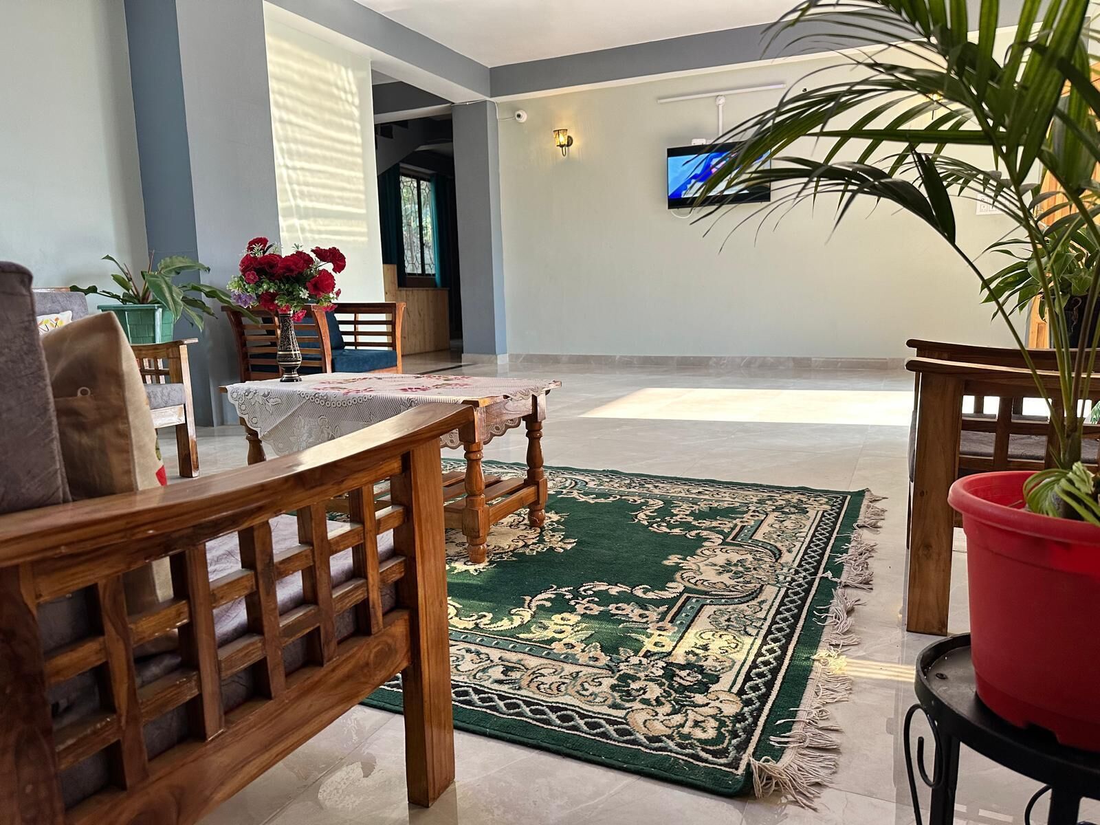 Un salón amplio con una mesa baja de madera, un tapete estampado verde y un televisor montado en la pared.