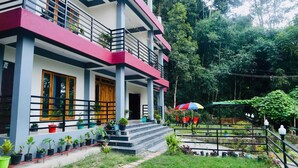 A two-story building with a balcony, potted plants, and a garden area with chairs and an umbrella. - The Grand Kalimpong (Kalimpong)