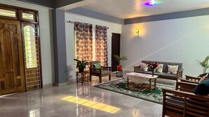 A spacious living room with a wooden door, a sofa set, a coffee table, and a potted plant. - The Grand Kalimpong (Kalimpong)