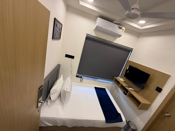 A hotel room with a bed, a TV, a ceiling fan, and an air conditioning unit. - Hotel Krisha, Dwarka (Dwarka)
