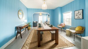 Una habitación amplia con una larga mesa de madera, paredes azules y un gran ventanal.