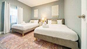 Habitación de hotel con dos camas, una alfombra estampada, una ventana con cortinas y una lámpara fijada a la pared.