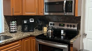 Una cocina con armarios de madera, microondas de acero inoxidable, estufa y cafetera.