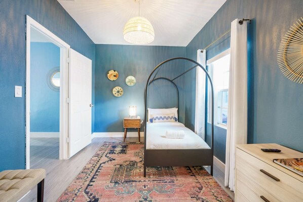Un dormitorio con cama, mesita de noche, cómoda, lámpara colgante y alfombra estampada.