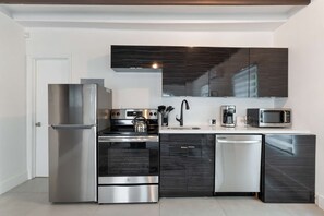 A modern kitchen with stainless steel appliances, dark cabinetry, and a white countertop. - Designer Studio | Close to Wynwood | Design District  | Downtown (Miami)
