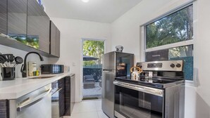 A modern kitchen with stainless steel appliances, a built-in oven, and a large window overlooking greenery. - Designer Studio | Close to Wynwood | Design District  | Downtown (Miami)